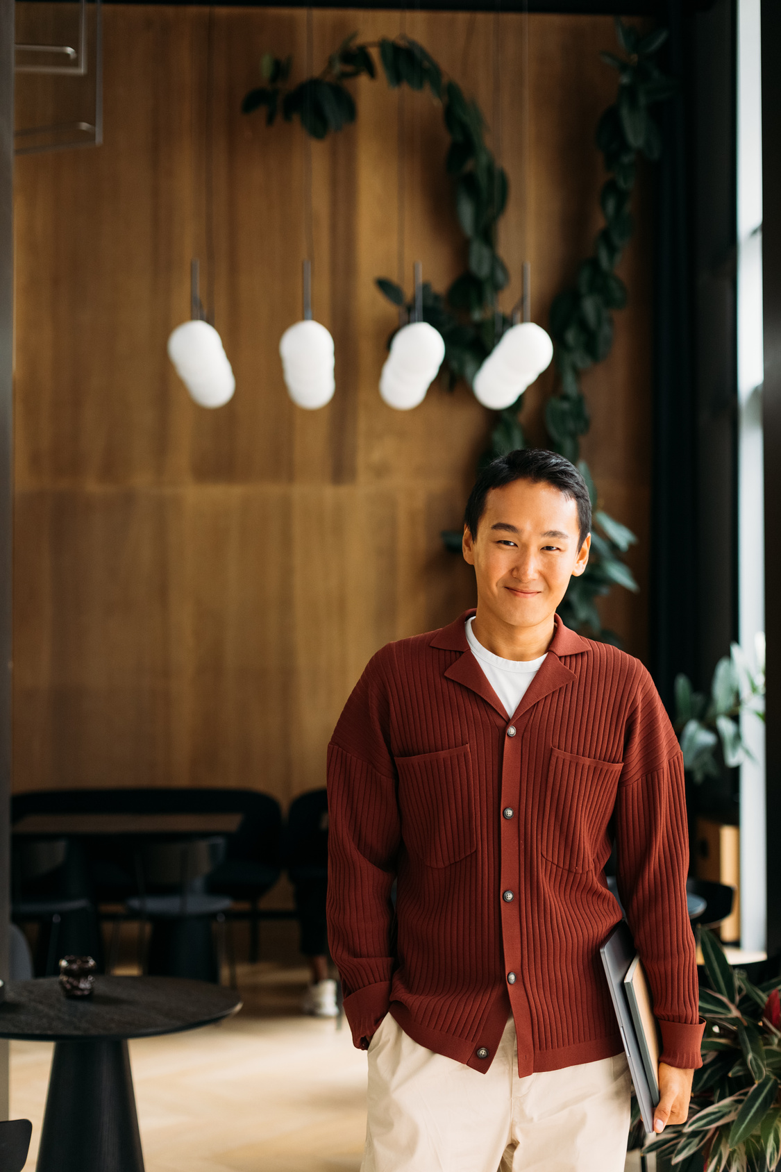 Young man in a red cardigan standing in a stylish restaurant interior with warm lighting