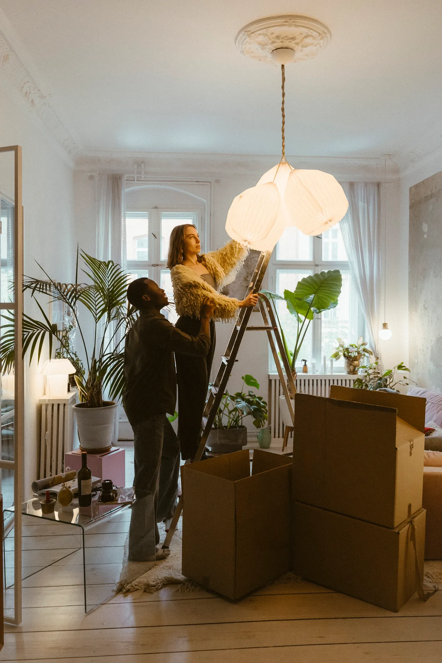 Couple unpacking moving boxes in a bright airy apartment while arranging artwork on a ladder