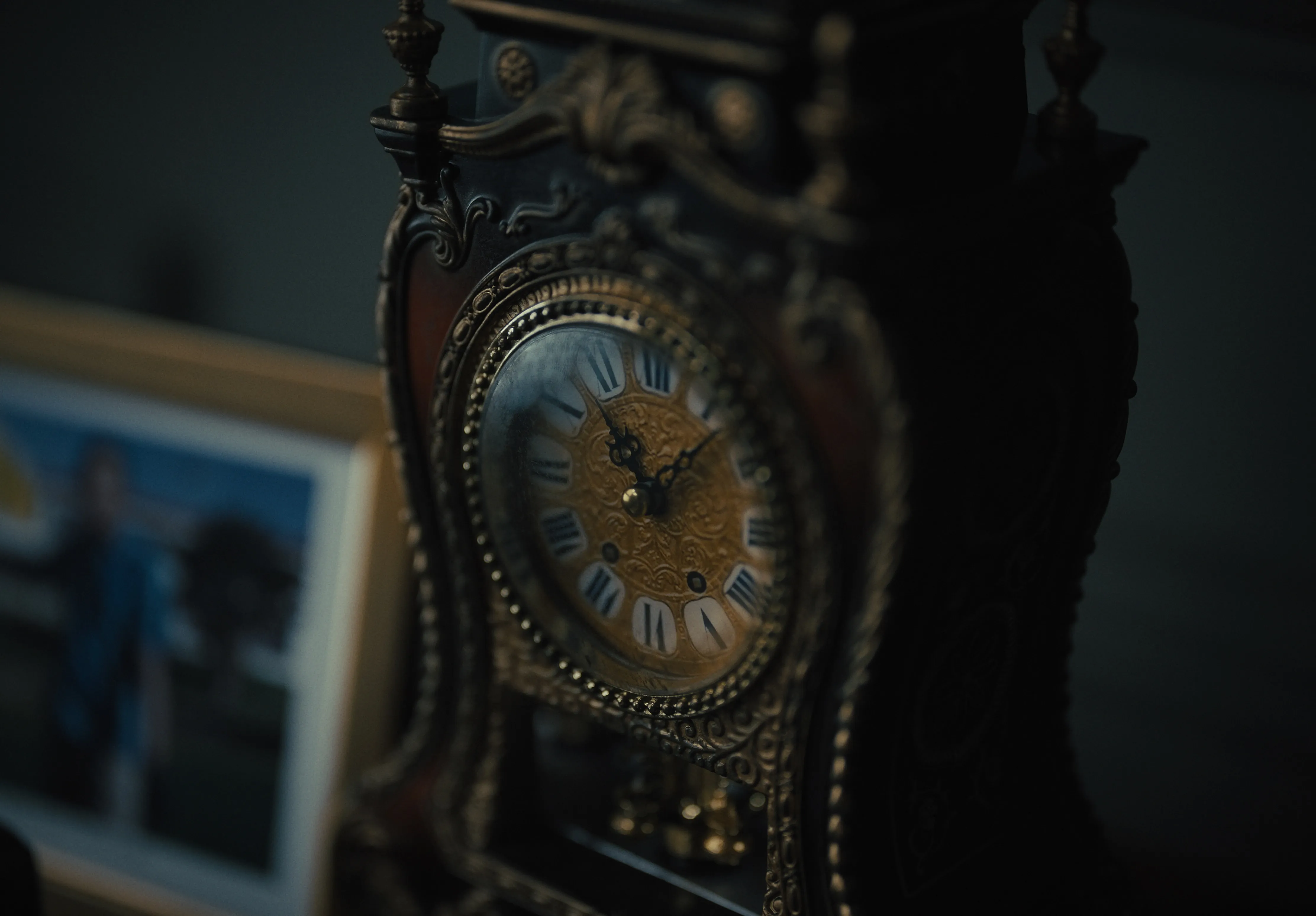 Traditional mantle clock with a pendulum and carved wooden casing in a dimly lit room.
