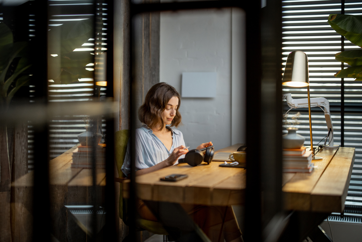 Woman sitting by a window in a dimly lit room working on her laptop