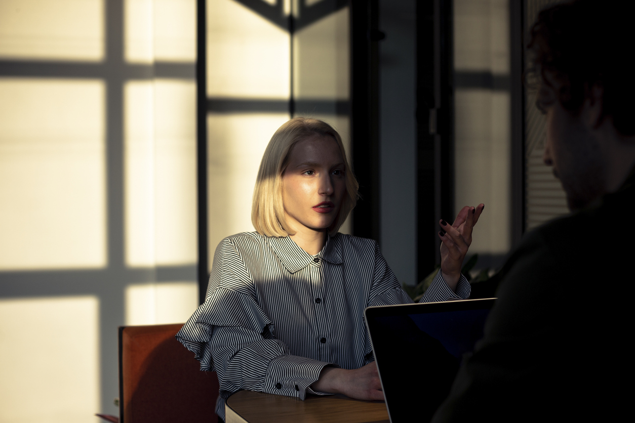 Young woman reading through documents at a table in a warmly lit room with blinds