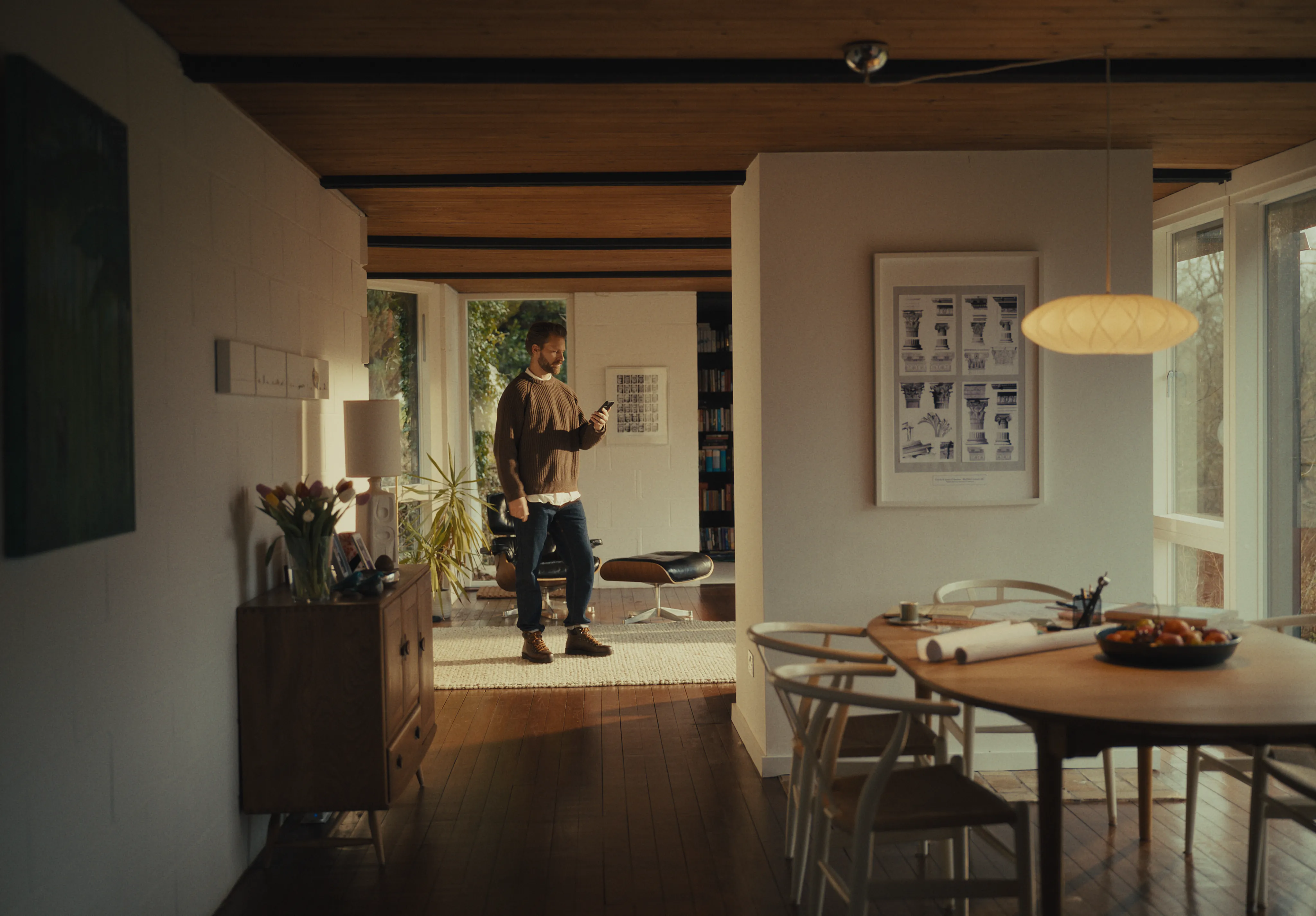 A man standing in a modern, mid-century living room looking at his smartphone.