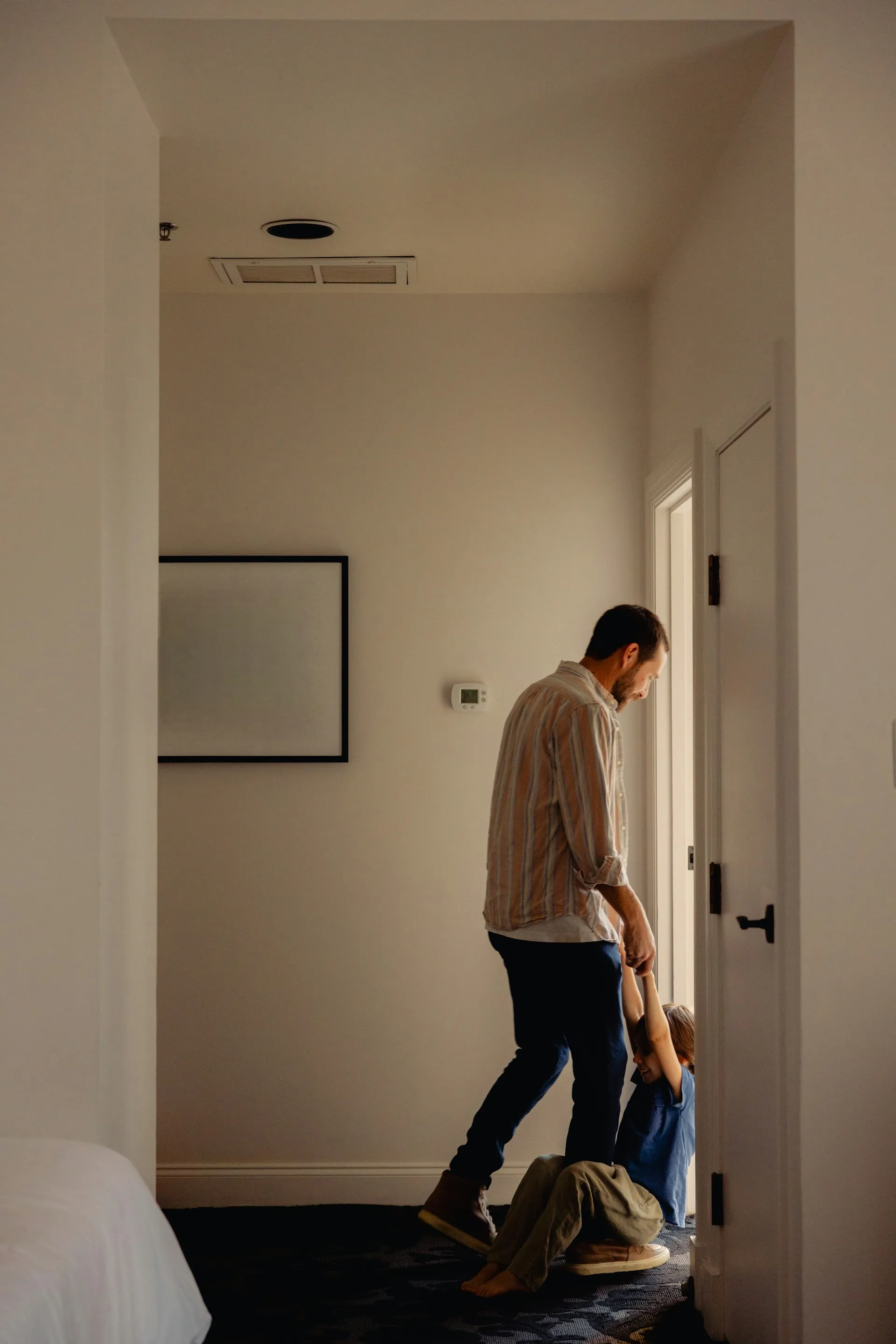 Man in a beige sweater walking through a hallway at home putting on his bag