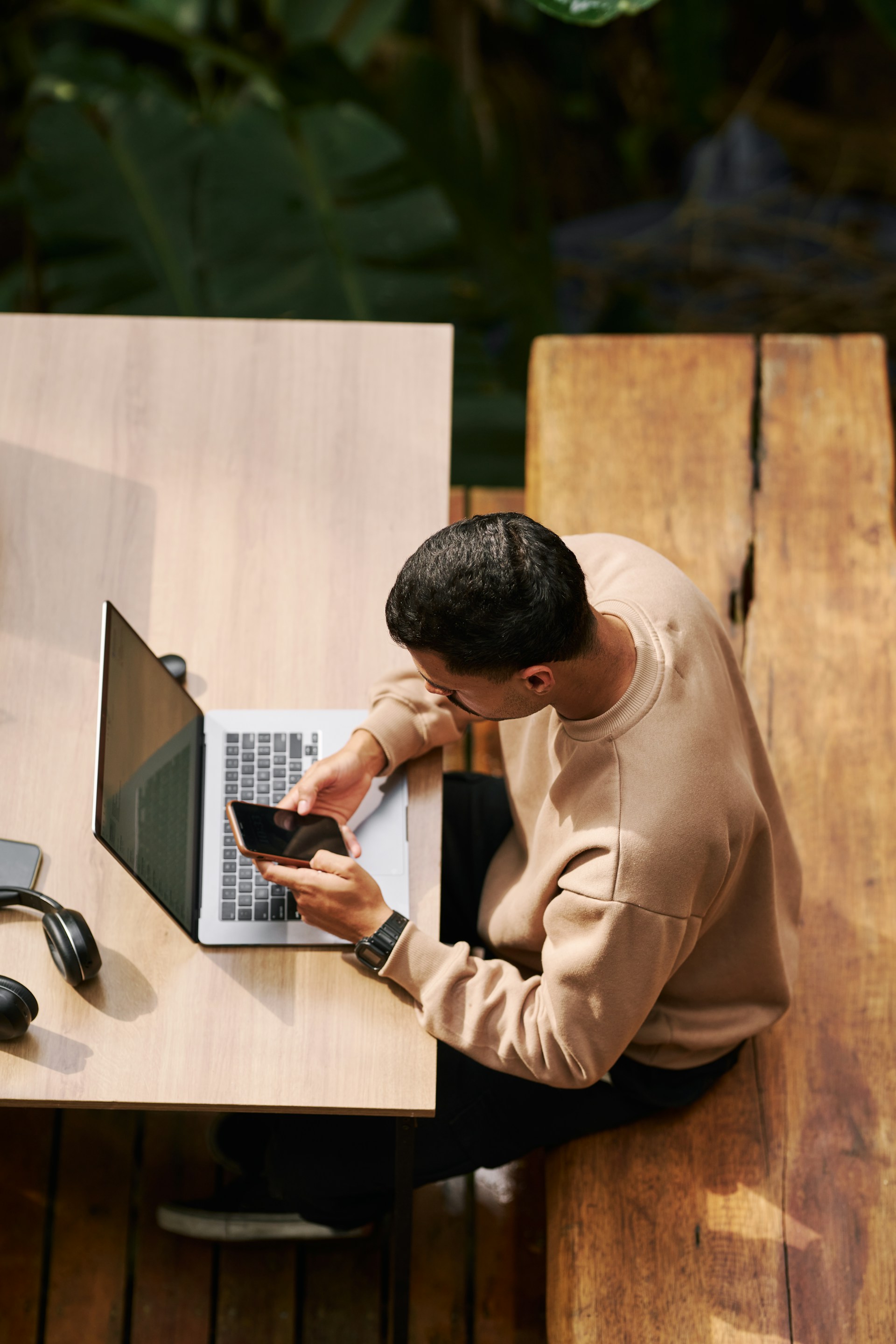 Young man checking his phone at a wooden desk with a laptop in a modern co-working space